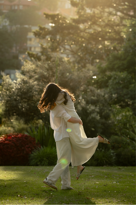 A woman holding a child in a park during sunset, with trees and greenery in the background.