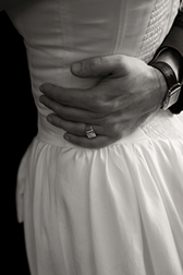 Close-up of a bride holding her wedding dress with both hands, showing a wedding ring on her left hand.