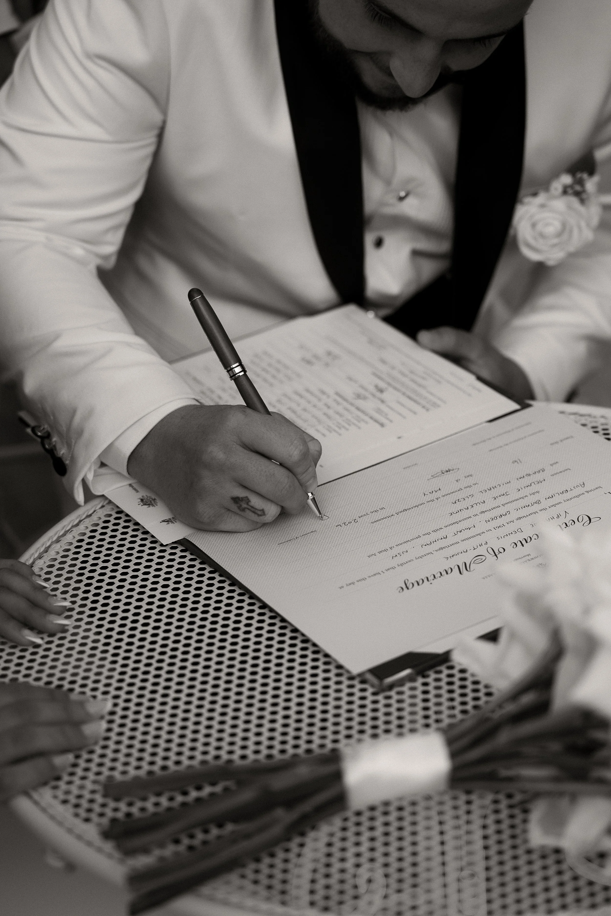 A groom signs his marriage certificate. He is wearing a white tuxedo.