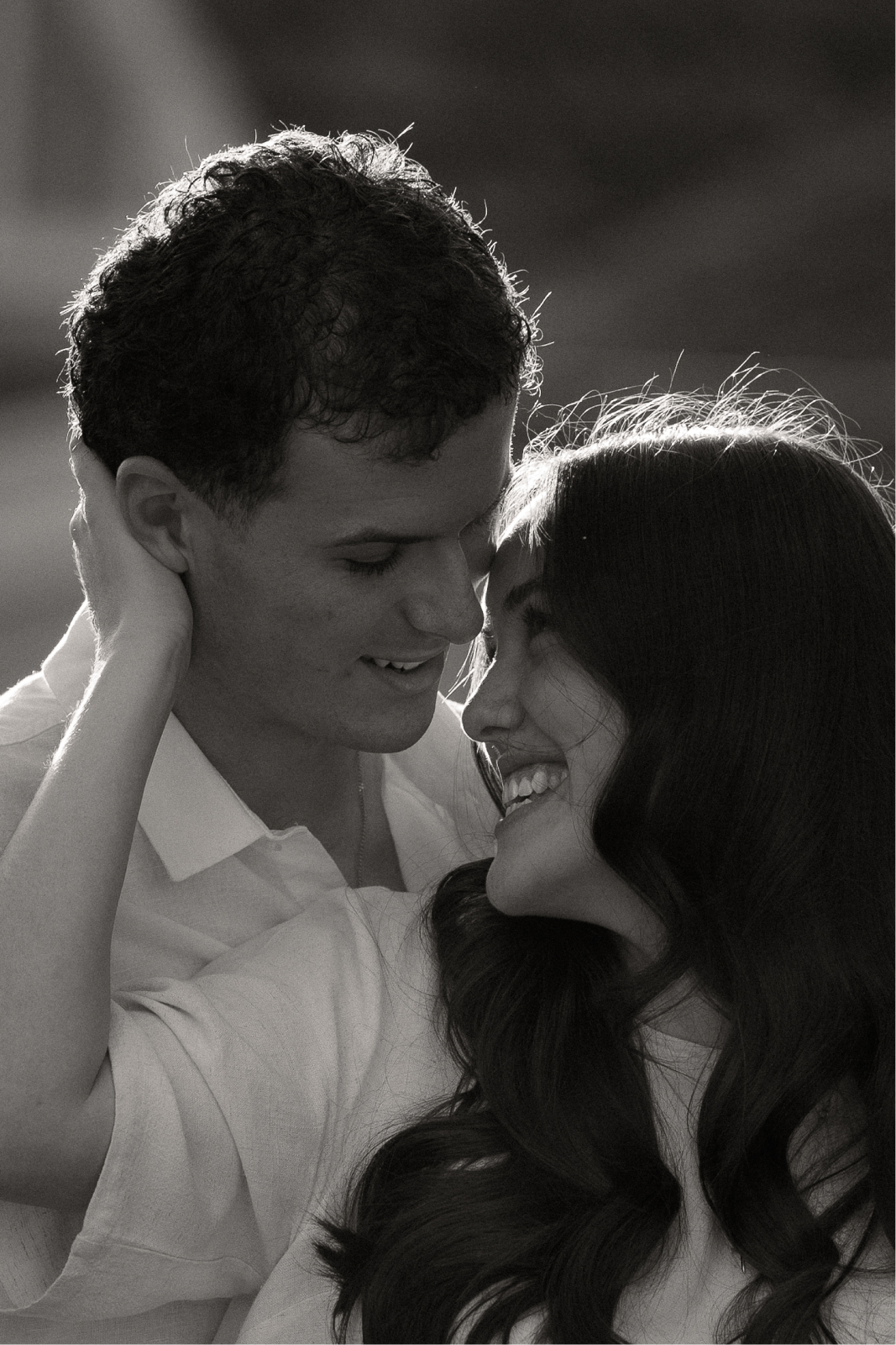 A black and white photo of a couple smiling and touching foreheads, appearing affectionate and happy.