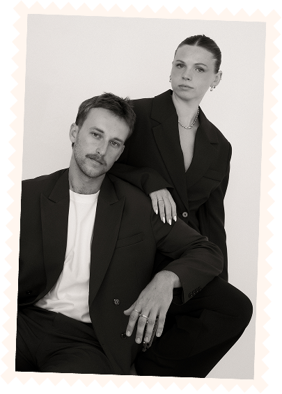 A man and a woman in black suits posing for a photo in a studio with a plain background.