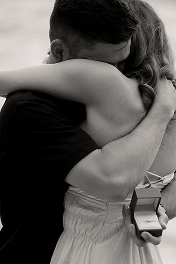 A couple hugging each other tightly while holding a cell phone.