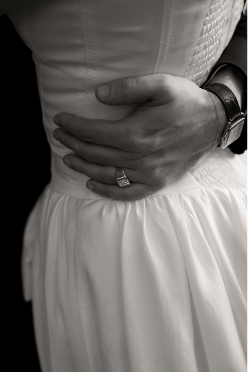 Close-up of a person in a white dress with hands crossed over their waist, wearing a ring and a watch.