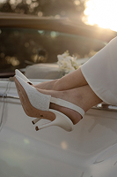 Feet wearing white high-heeled shoes resting on a car hood