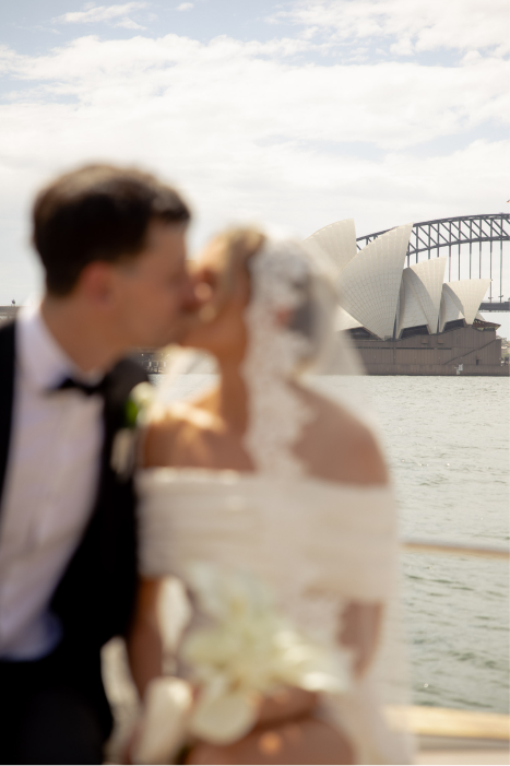 Blurred image of a bride and groom kissing near Sydney Opera House and Harbour Bridge.