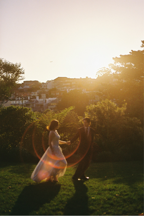 A couple dancing outdoors during sunset with buildings in the background.