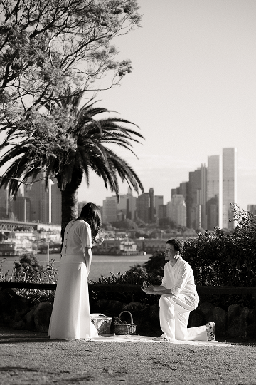 A man proposing marriage to a woman in a park with the city skyline in the background, black and white photo.
