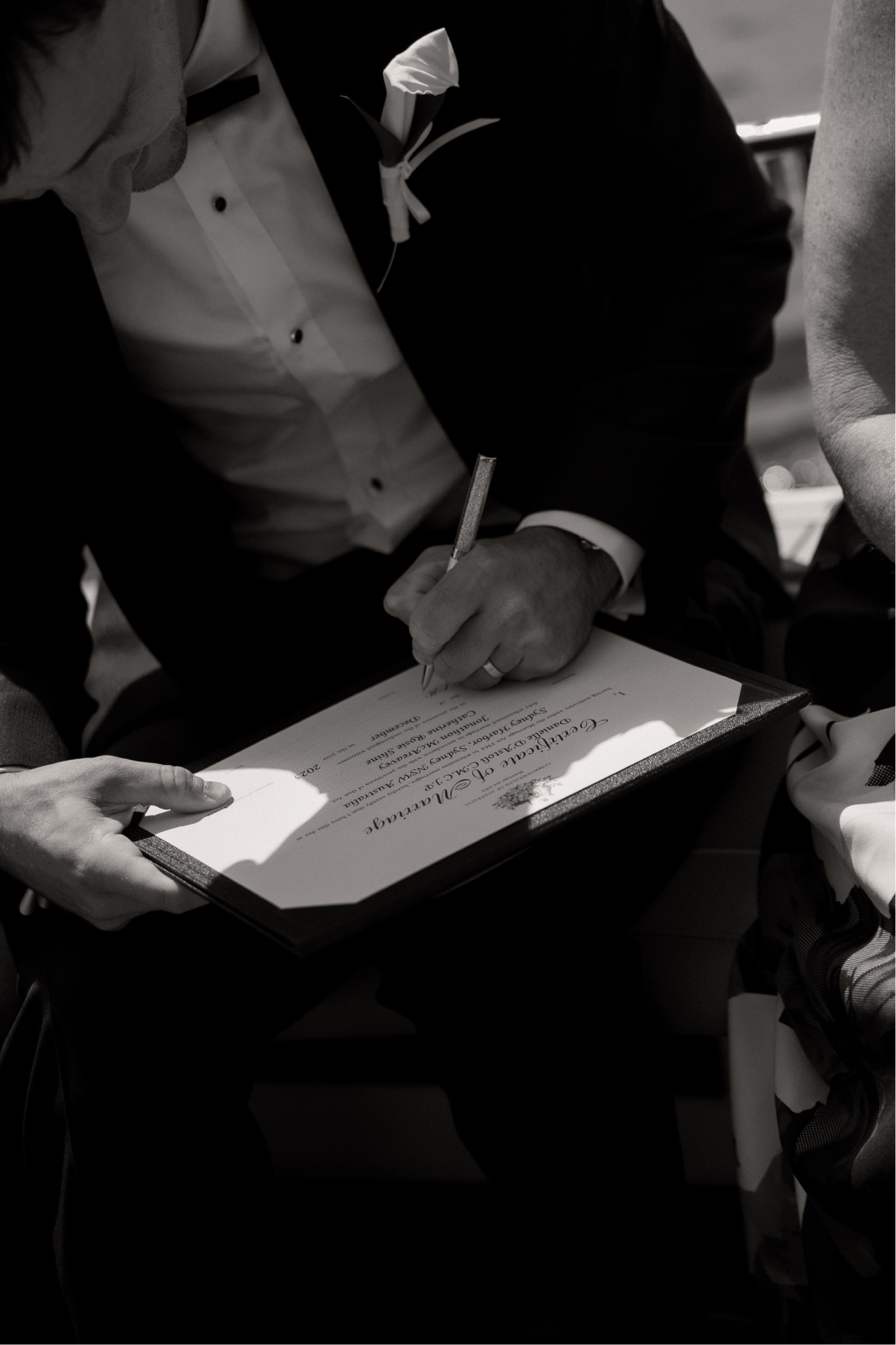 A person signing a wedding certificate while another person holds it, at a wedding ceremony.