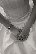 Close-up of a person wearing a white dress, sitting with hands clasped in their lap, holding a bouquet.