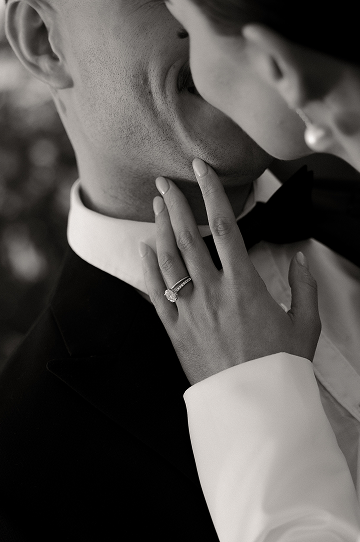 Close-up of a bride and groom sharing a kiss, with the bride's hand showing an engagement ring, in black and white.