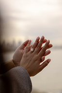 Hands of a person with a ring on their finger, reaching out over a body of water at sunset.