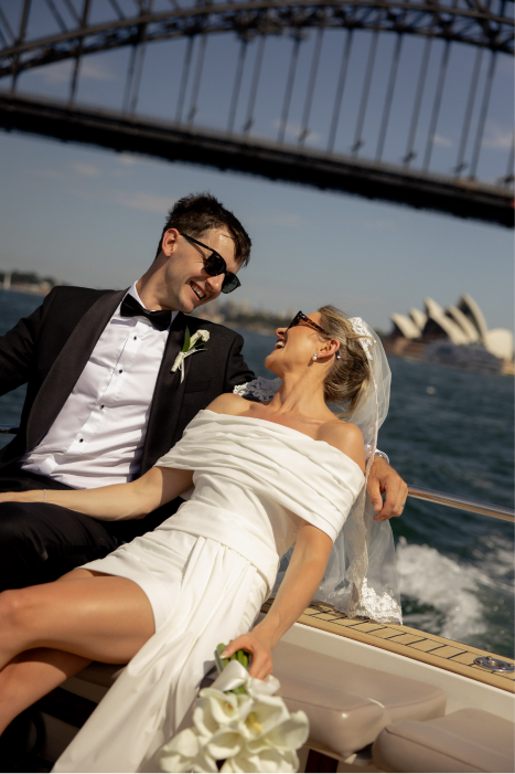 A newlywed couple on a boat, with the Sydney Harbour Bridge and Opera House in the background, during daytime.