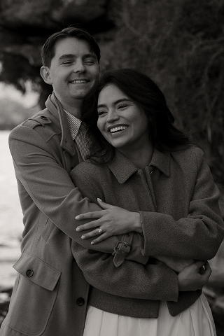 A smiling man and woman embracing outdoors in black and white.