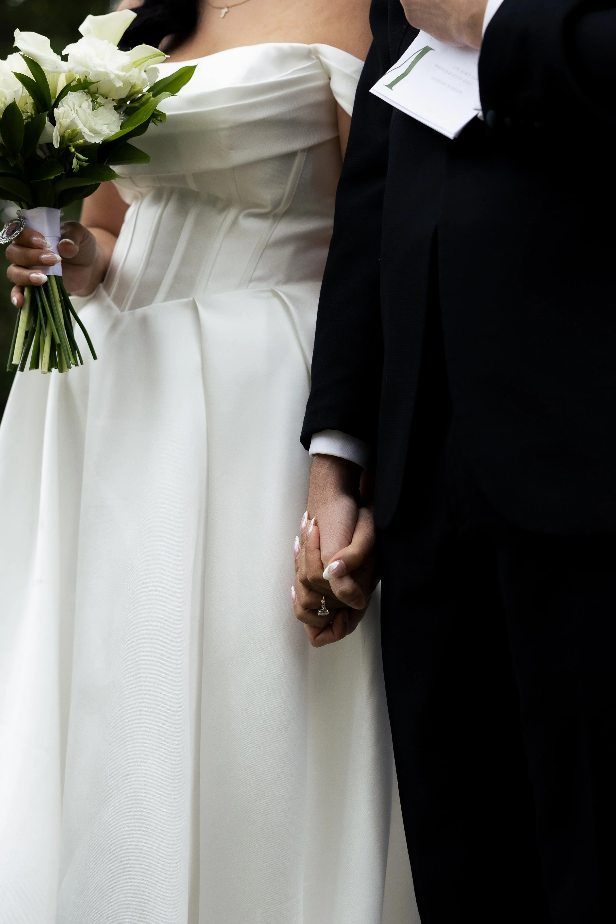 Close-up of a bride and groom holding hands during their wedding ceremony, with the bride holding a bouquet of white flowers.