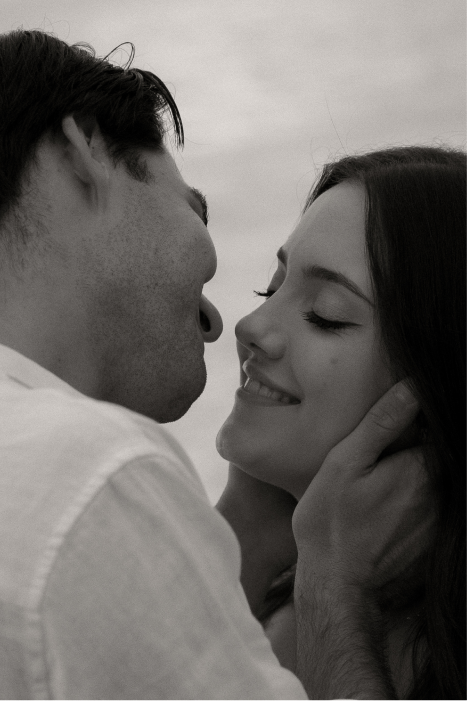 A couple sharing an intimate moment, about to kiss, with the man gently holding the woman's face and both smiling.