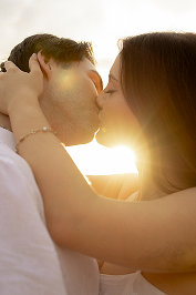 A couple kissing outdoors with sunlight in the background.