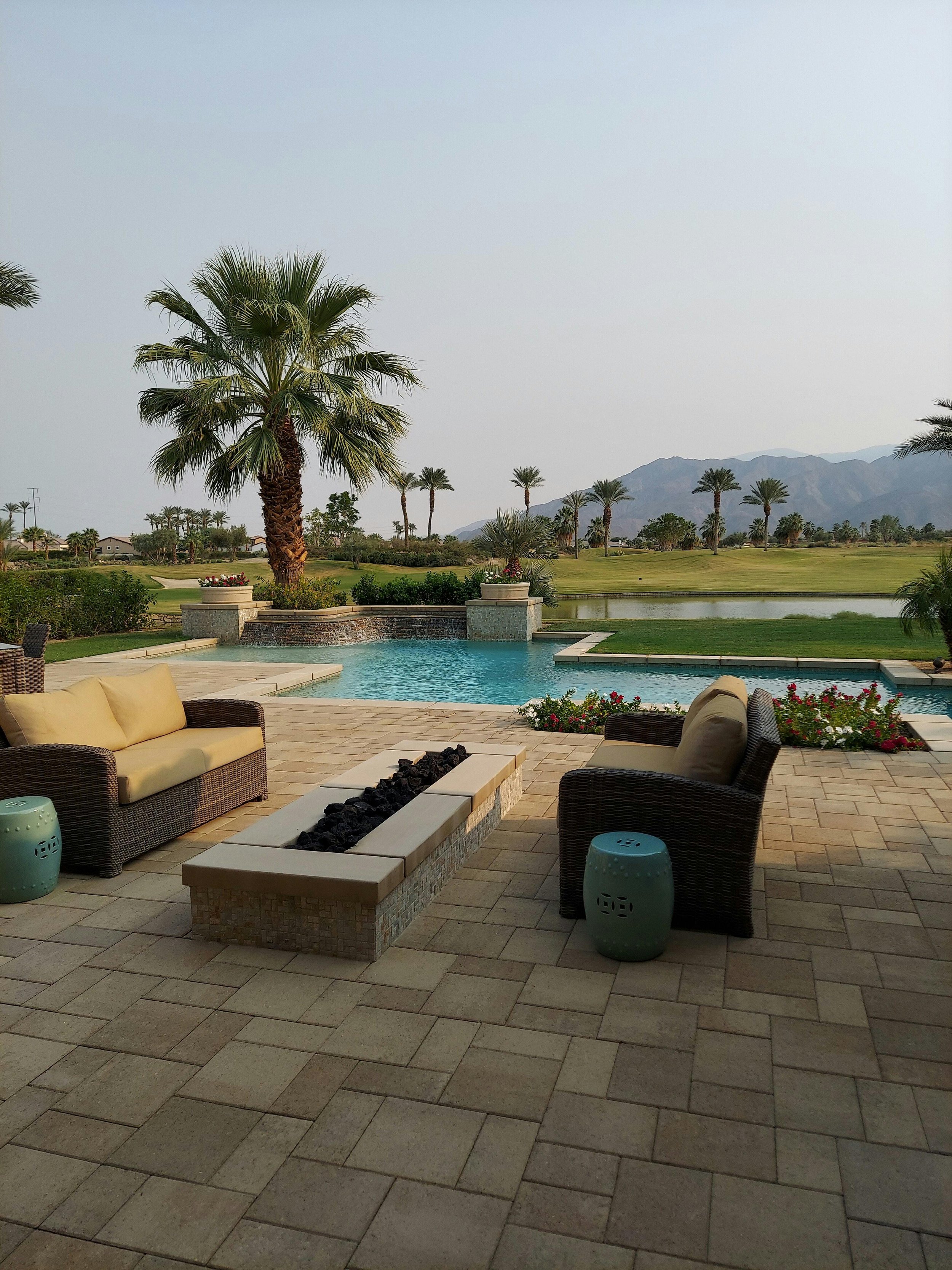 Outdoor patio with wicker furniture, a fire pit, and a view of a golf course, palm trees, and distant mountains.