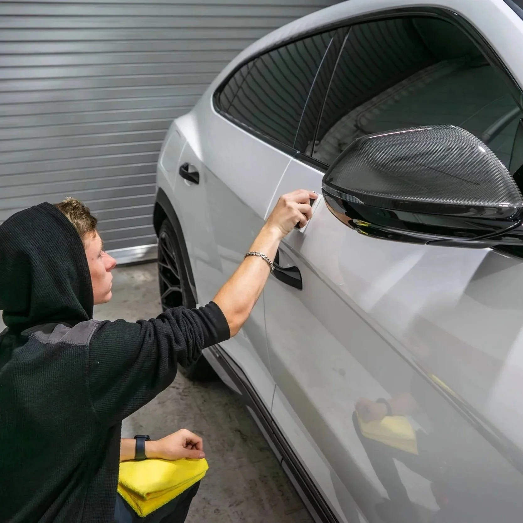 Auto detailing technician polishing and correcting paint on a white vehicle door near the side mirror during professional paint correction service.