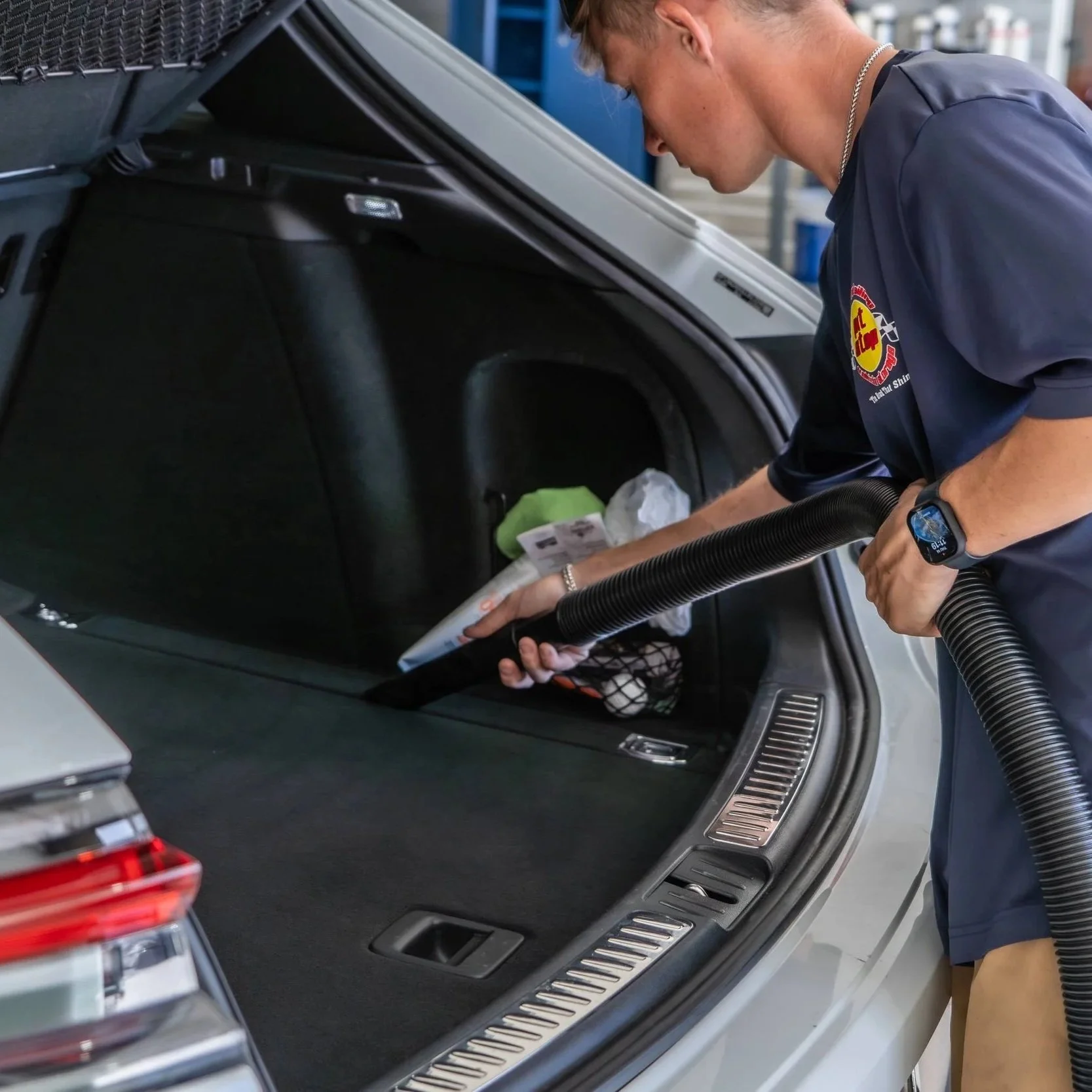 Professional detailer cleaning a car’s trunk with a vacuum hose, removing desert dust as part of leather interior cleaning and conditioning service.