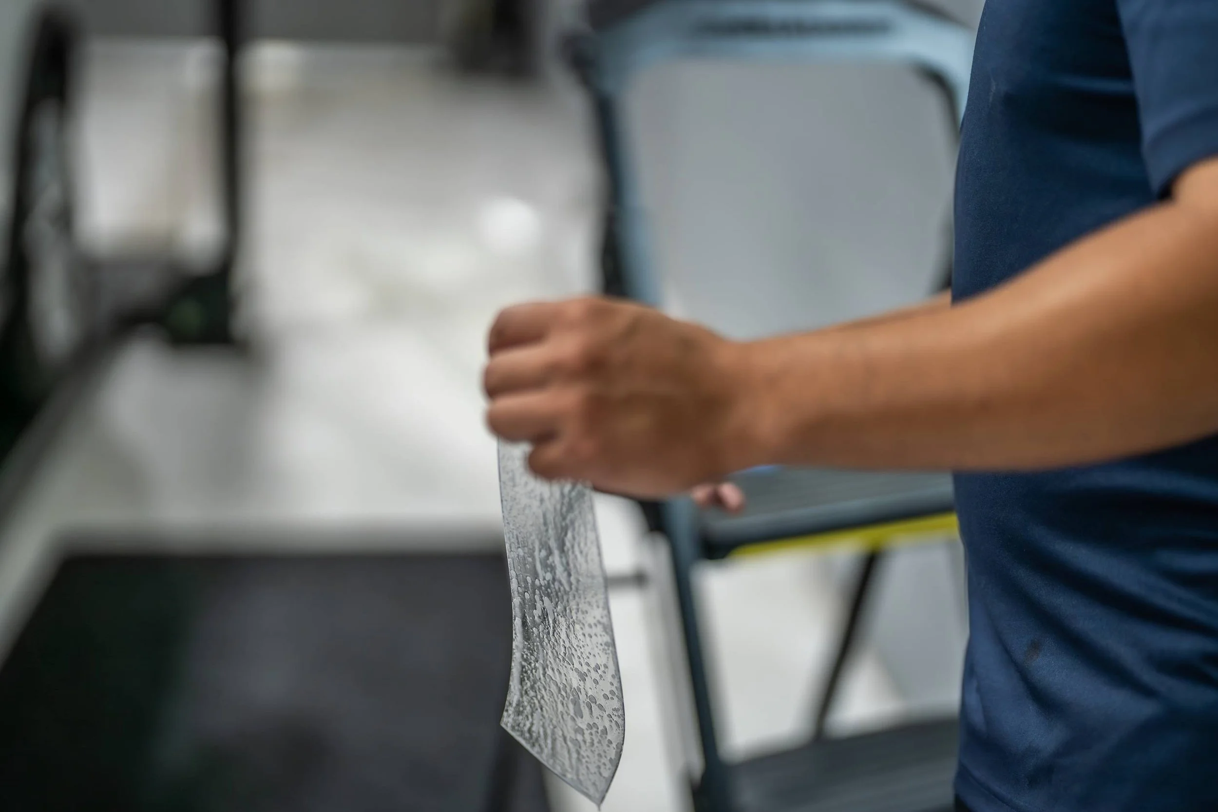 A person holding a wet, semi-transparent knife blade in a commercial kitchen or food preparation area.