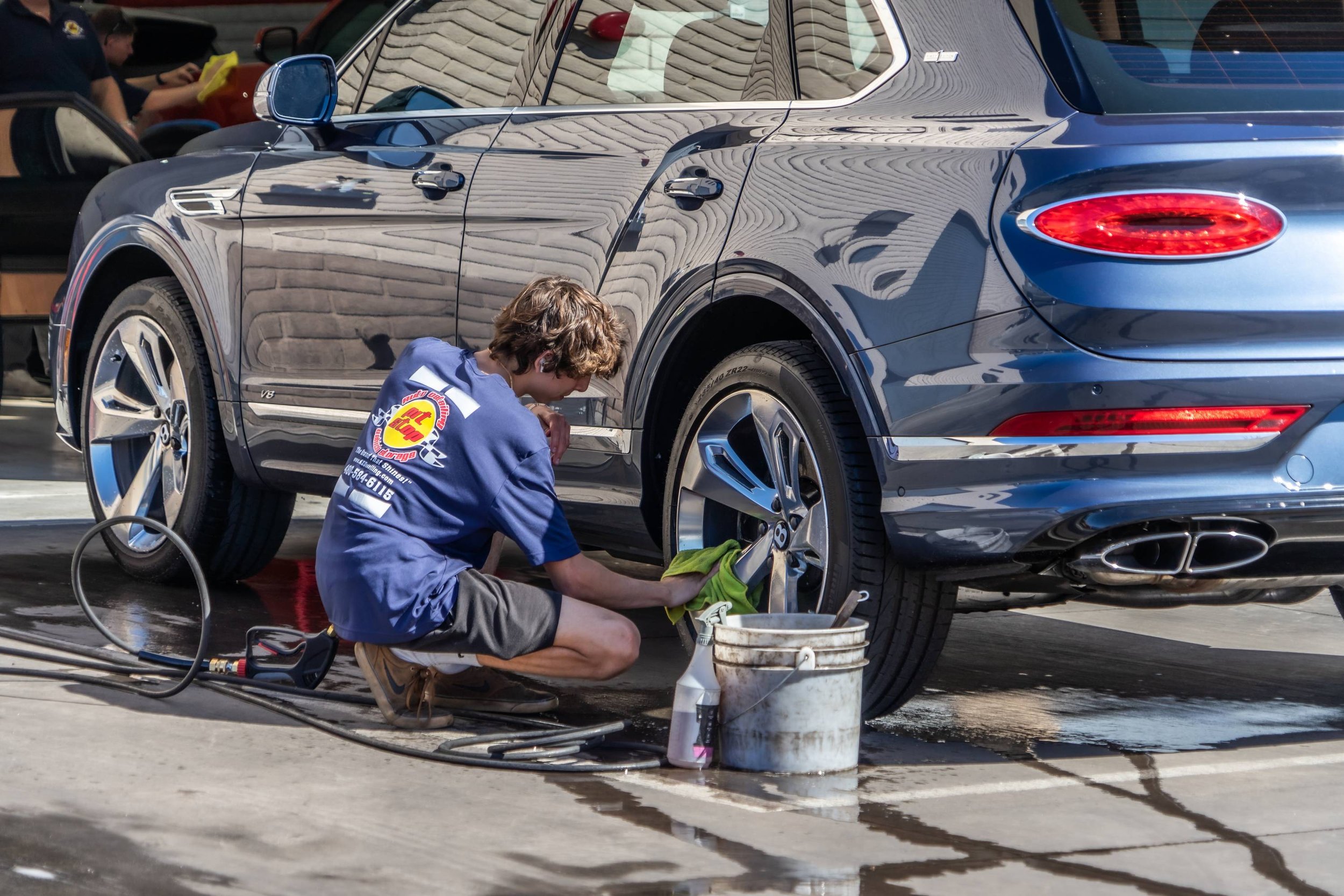 A person cleaning the wheel of a luxury blue car at a car wash or detailing station.