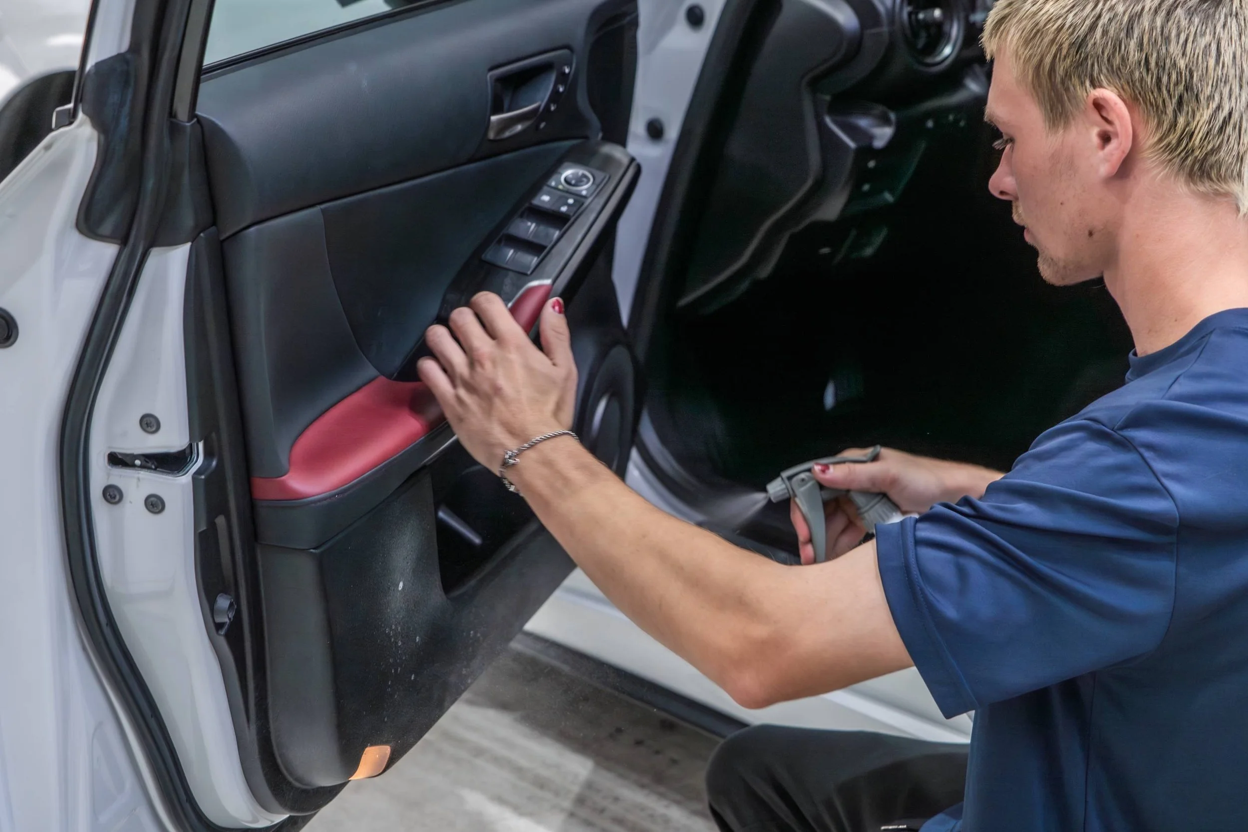A woman is cleaning the interior of a car door with a handheld vacuum cleaner.