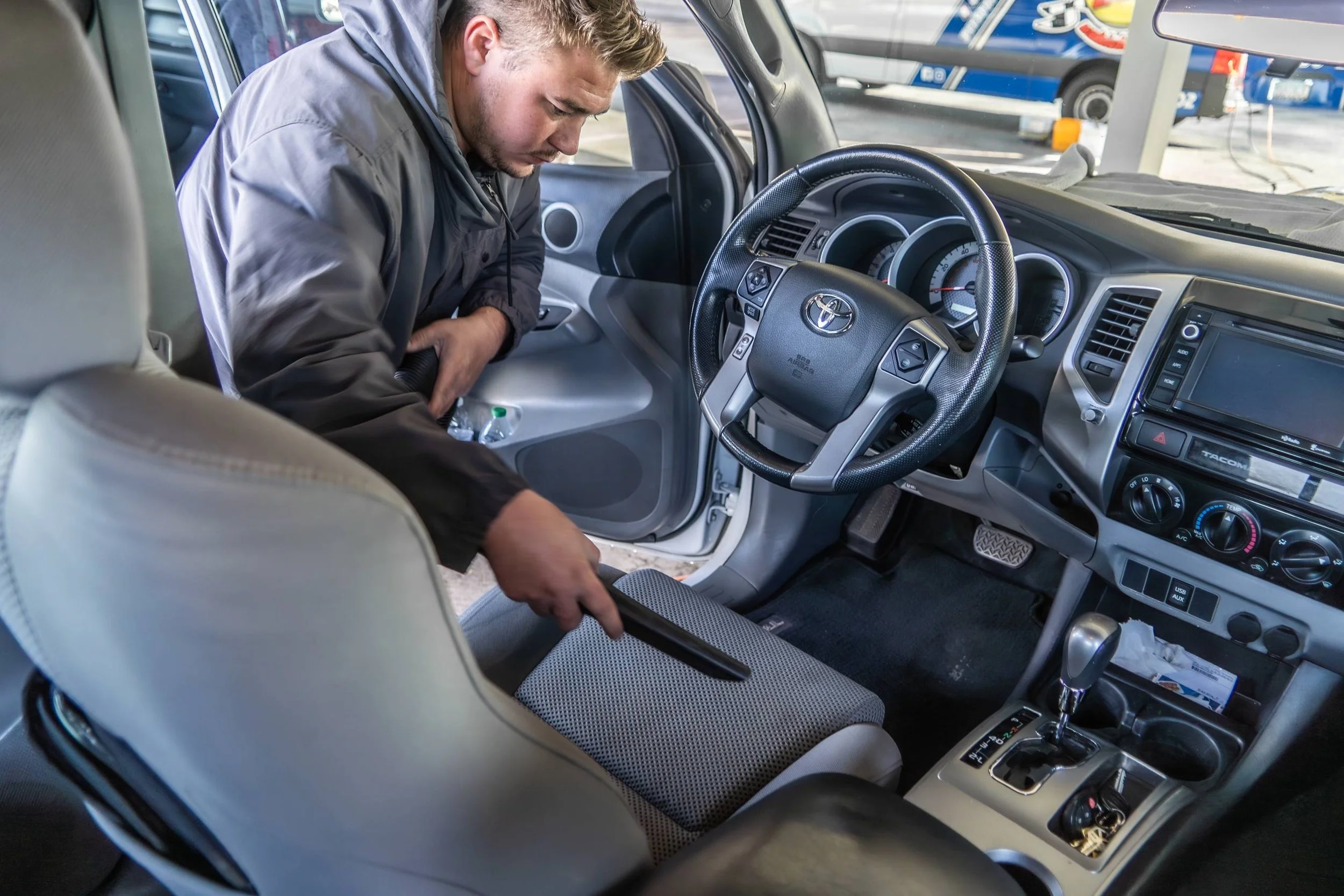 A man vacuuming the front passenger seat of a Toyota Tundra truck inside a parking garage.