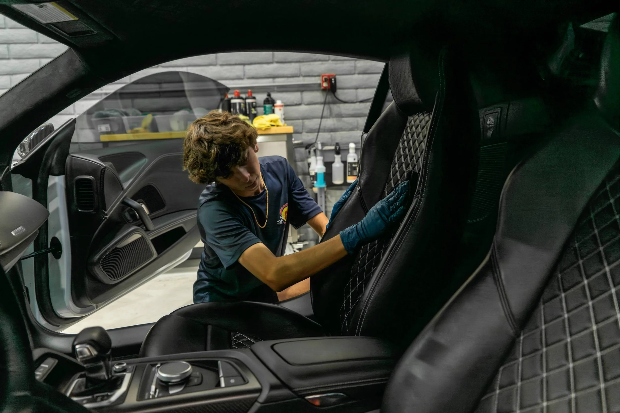 A person cleaning the interior of a car with black leather seats inside a garage.