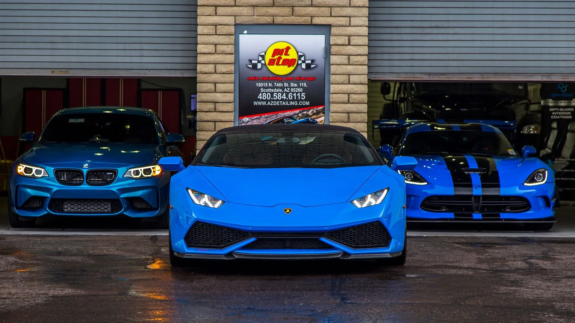 Three blue luxury cars parked in front of an auto detailing shop, with a sign above them displaying the shop's name and contact information.
