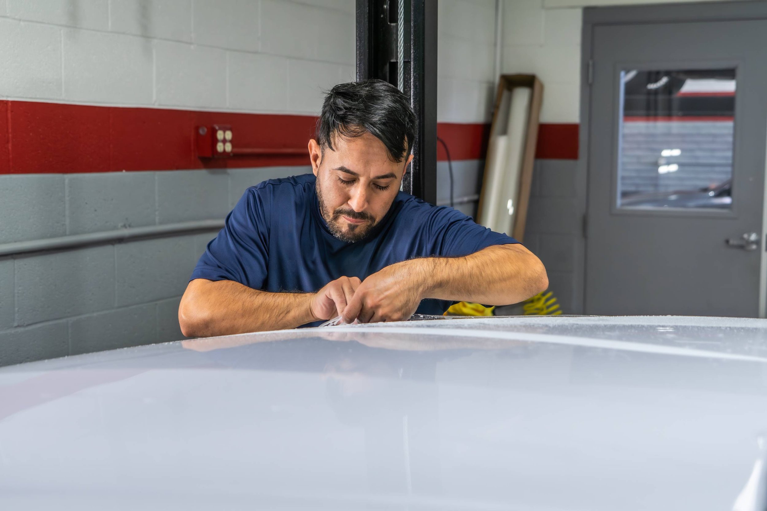 A man working on the hood of a white car in a garage or workshop.