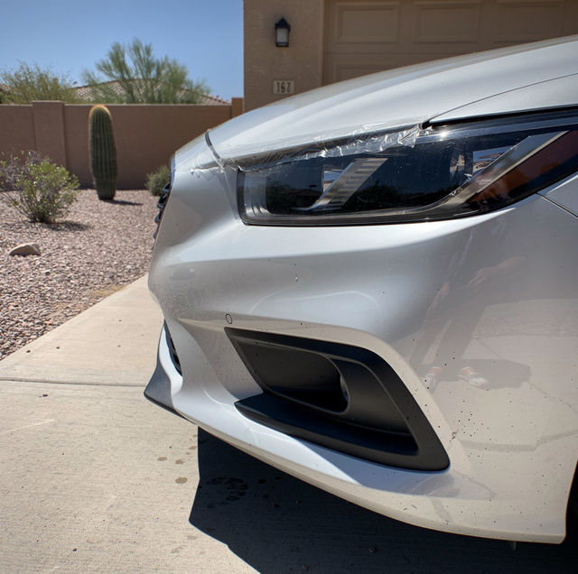 White car parked in driveway with cactus and desert landscaping behind brown fence.