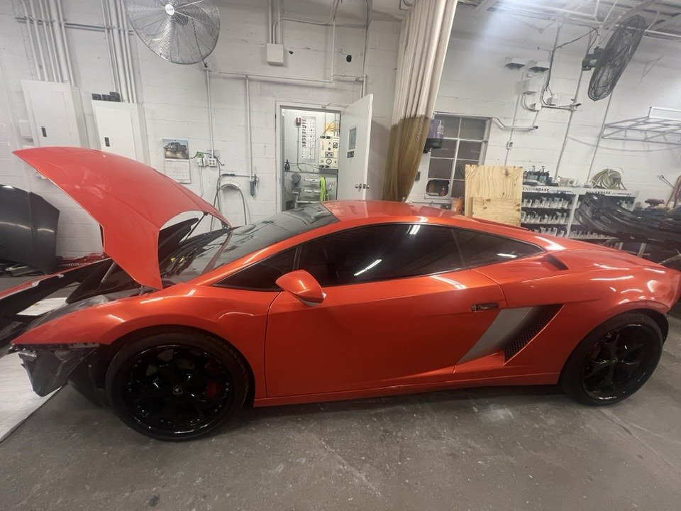 Red sports car in a garage with the hood raised and black wheels.