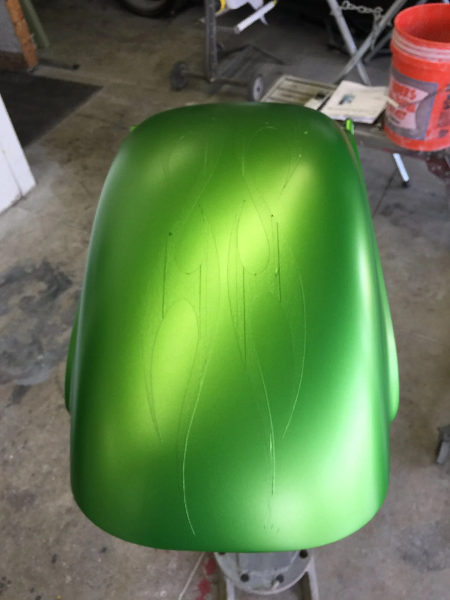 Green painted object with light-colored thin line designs on it, placed on a stand in a workshop setting.
