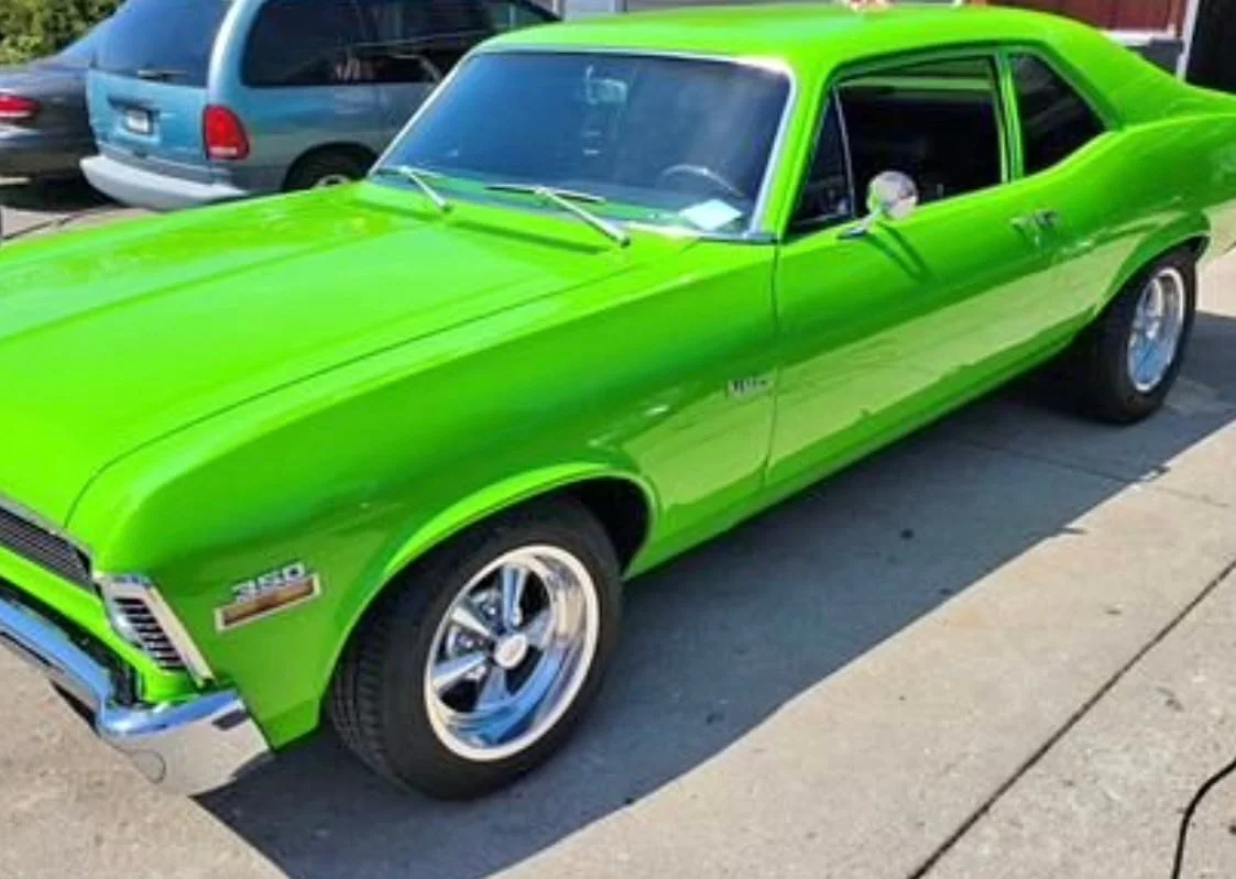 A bright green vintage muscle car parked on the street with other vehicles in the background.