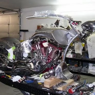 Unfinished motorcycle frame and engine in a workshop with tools and parts on a workbench.