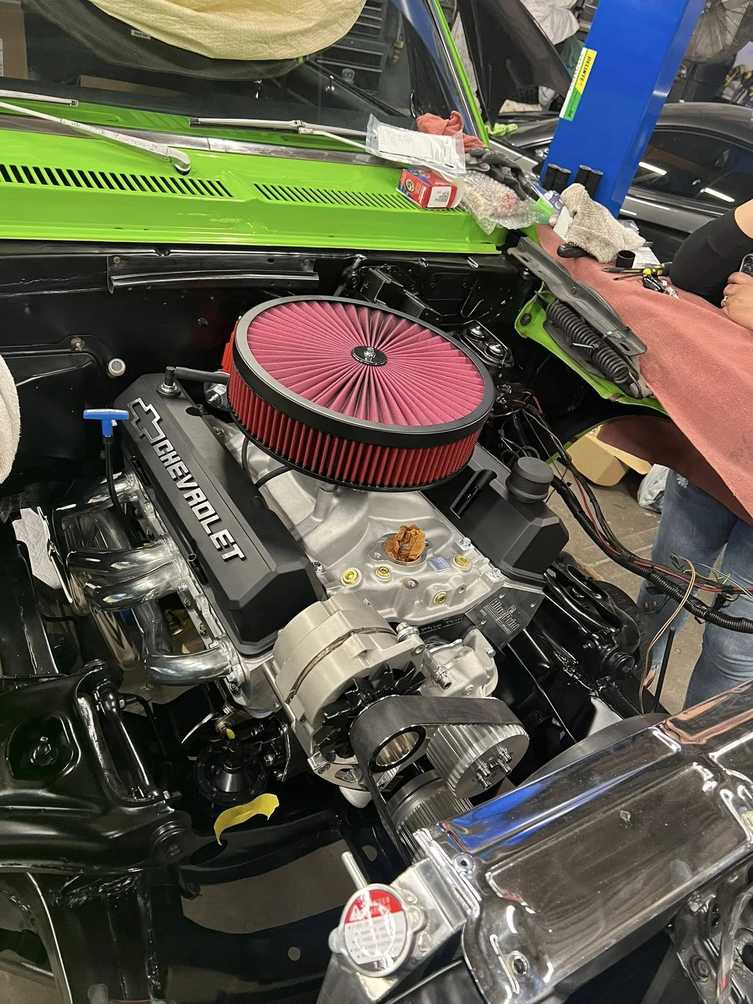 A car engine being assembled with a pink air filter, Chevrolet valve covers, and various tools and parts spread around.