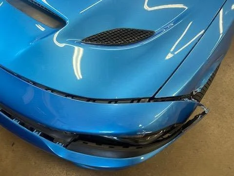 Close-up of the front bumper and hood of a blue sports car with visible damage to the front right corner.