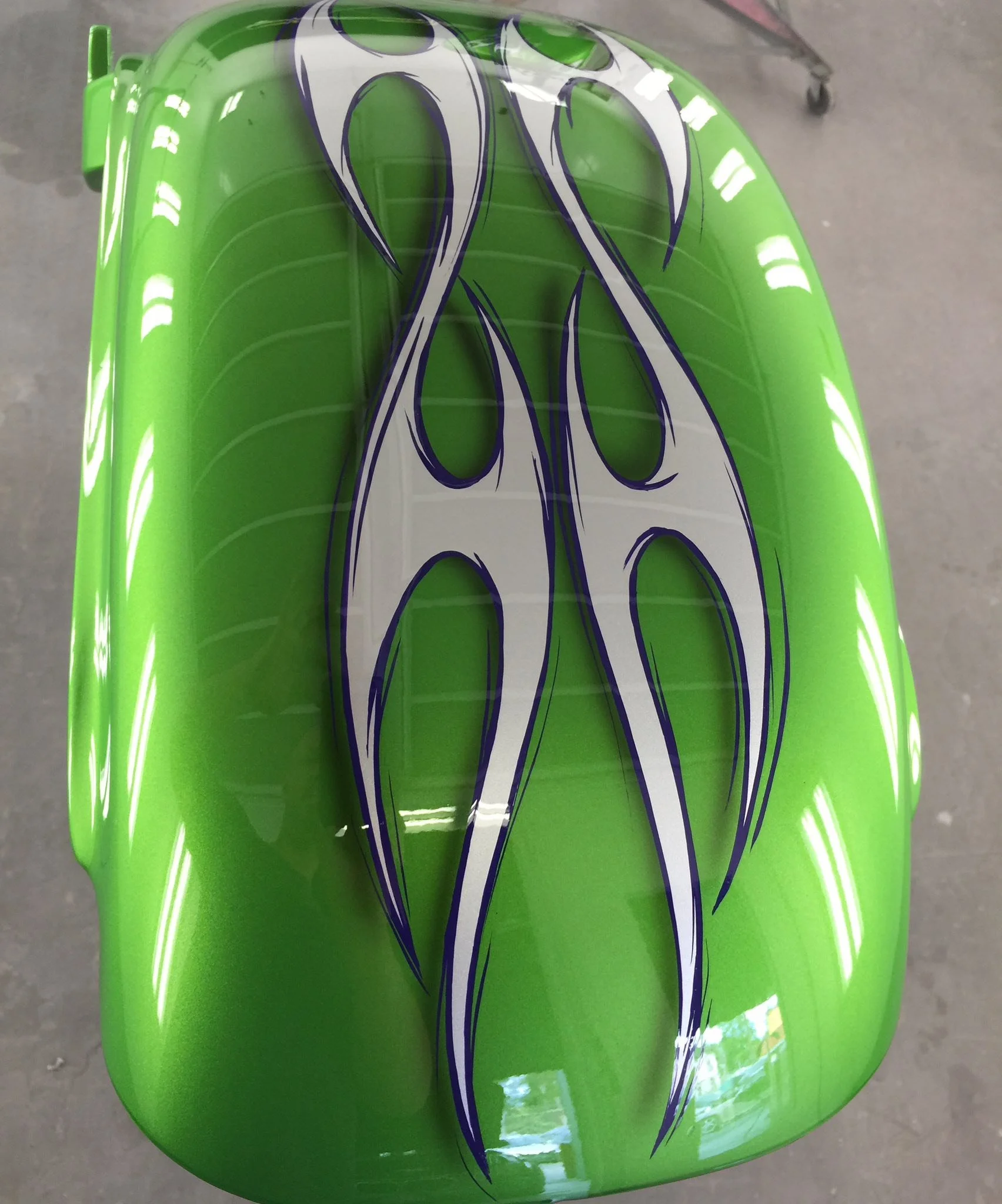 Close-up of a green motorcycle gas tank with white and blue flame decal design.