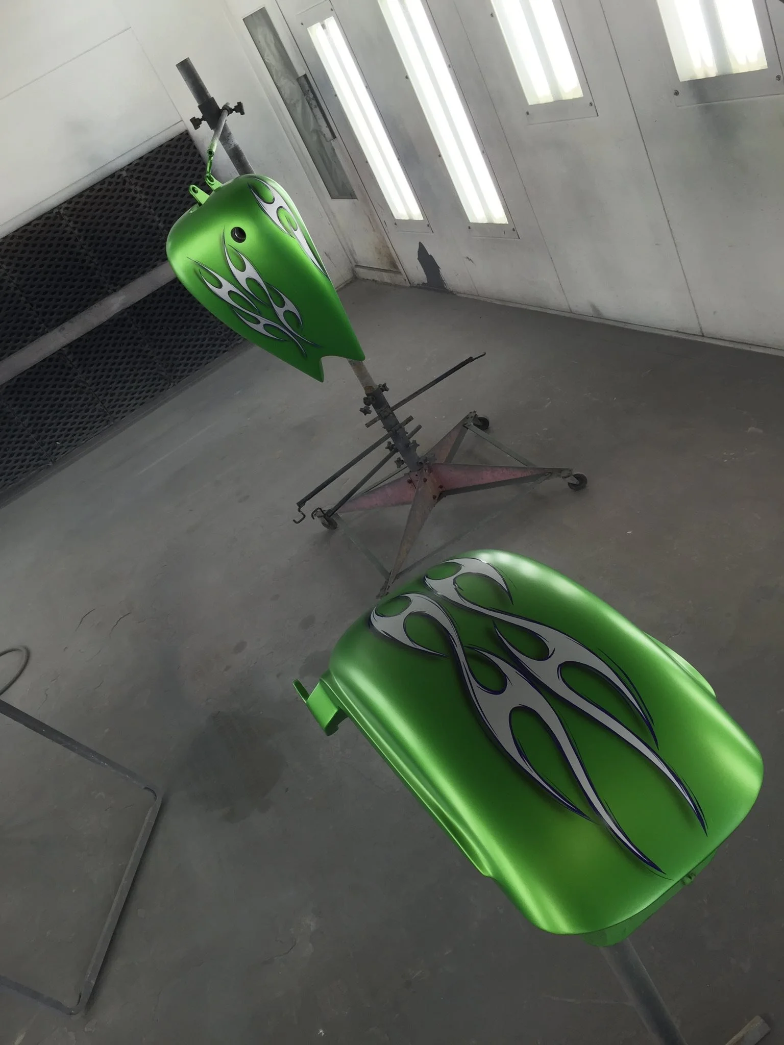 Green motorcycle fuel tank and seat with flame decal being painted in a spray booth.