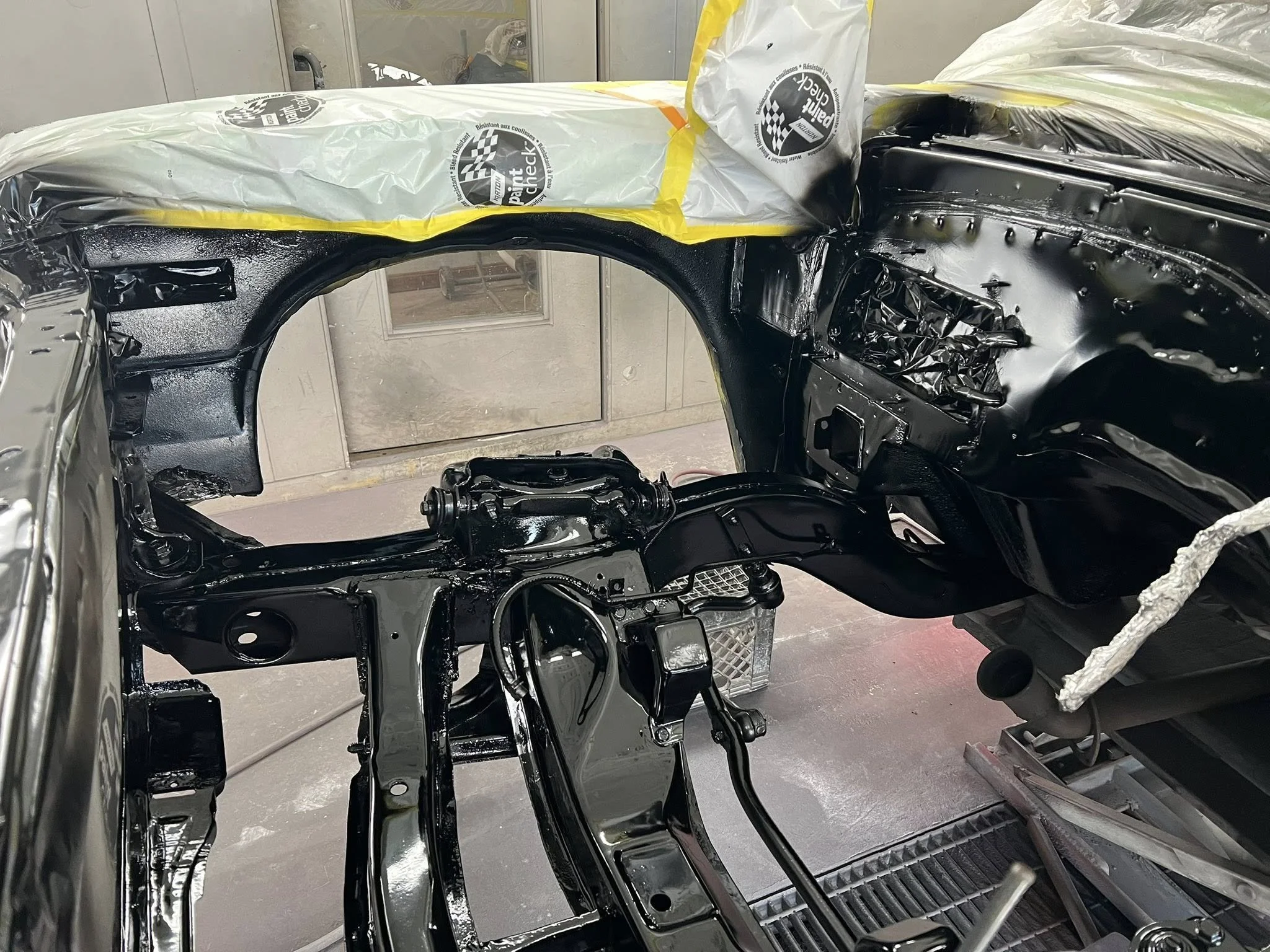 The interior of a car chassis being painted black inside a workshop.