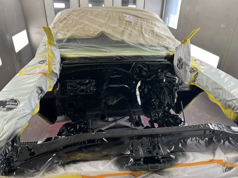 Car in a paint booth with masked and masked parts, and paint supplies visible.