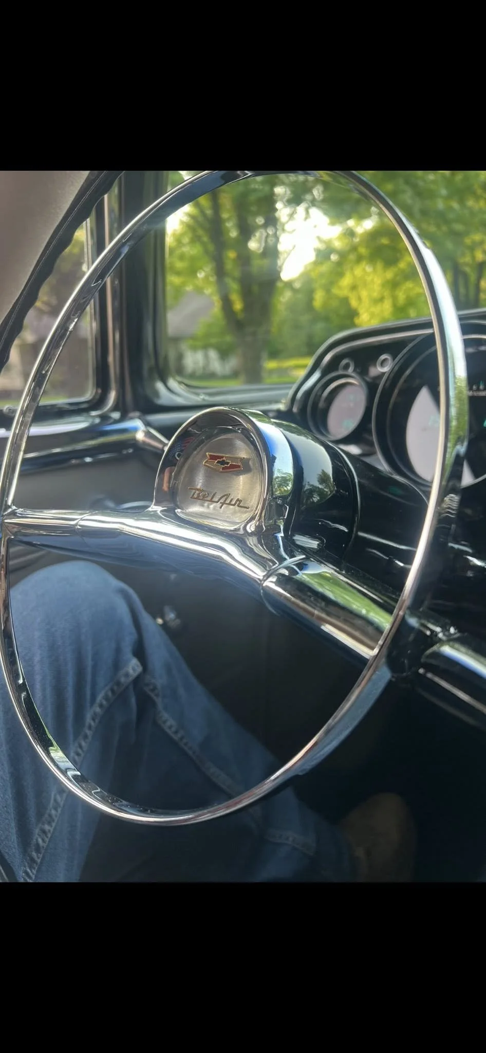 Interior view of a vintage Chevrolet truck with a shiny steering wheel and dashboard, with a scenic view of trees through the windshield.