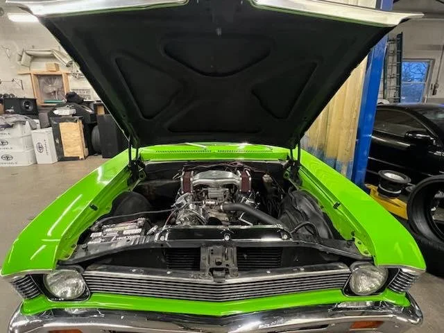 Front view of a bright green classic car with its hood open, showcasing the engine in a garage.