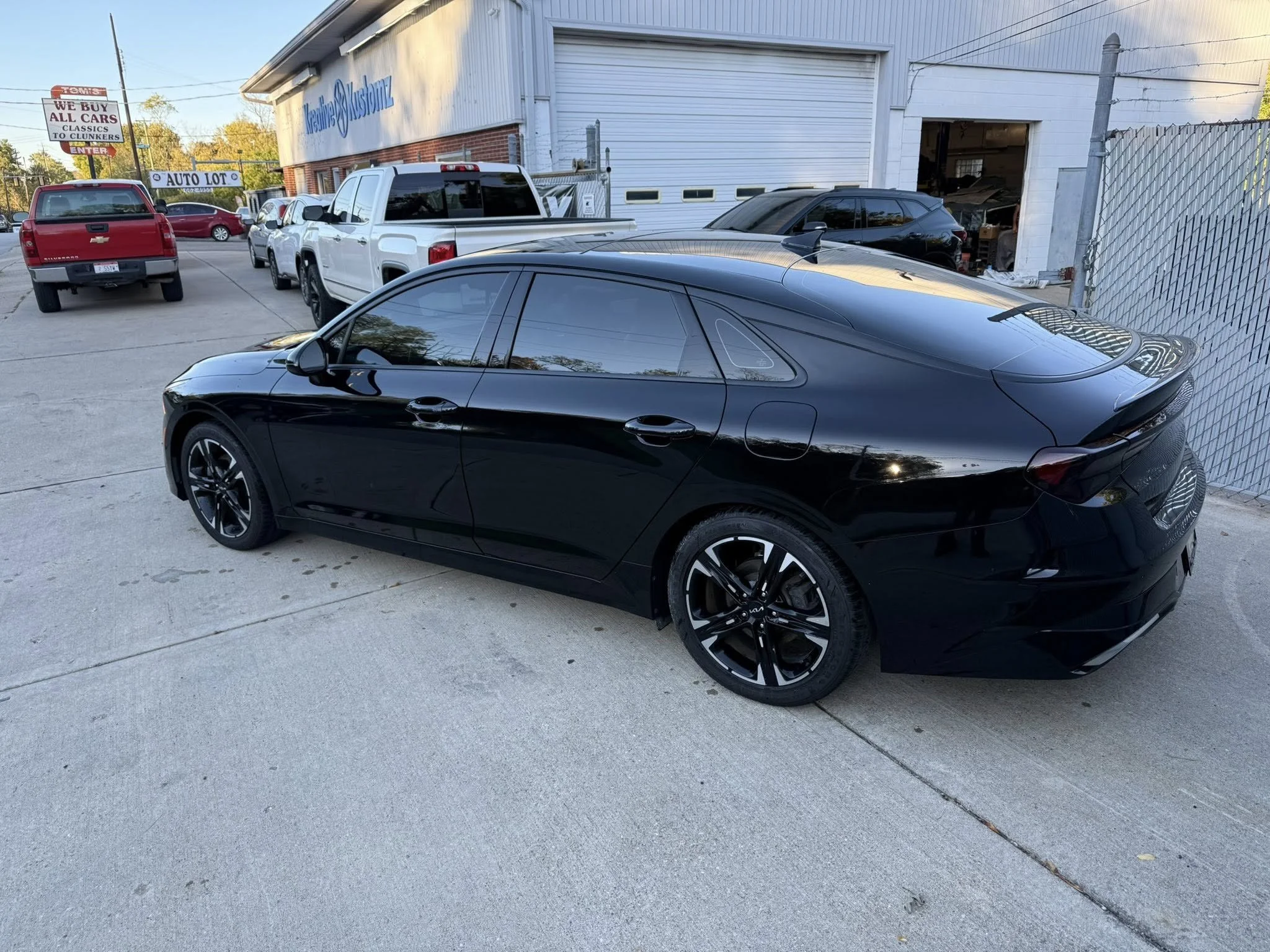 Black sedan car parked outside a building with a white garage door, surrounded by other vehicles in a parking lot.