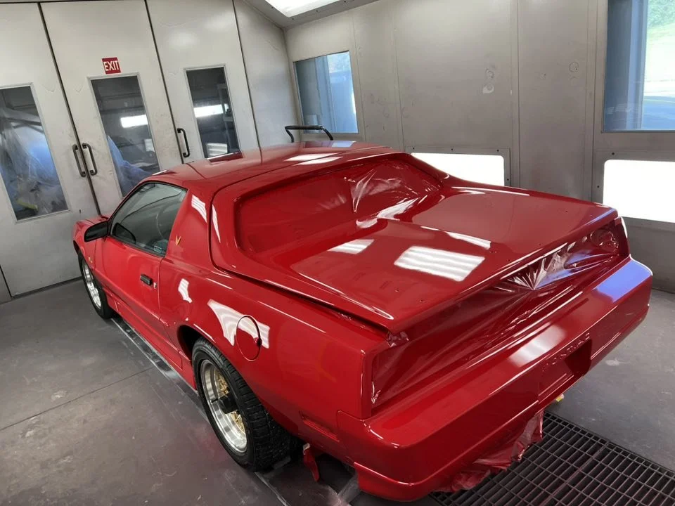 A red vintage sports car inside a garage or paint booth.