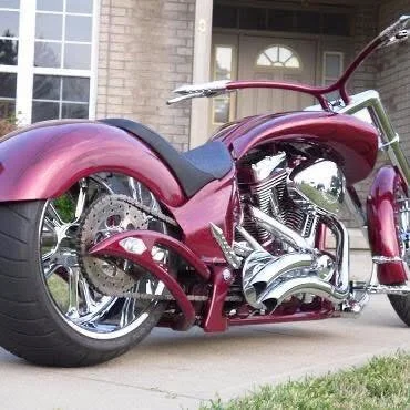 Pink motorcycle parked on a sidewalk in front of a house.