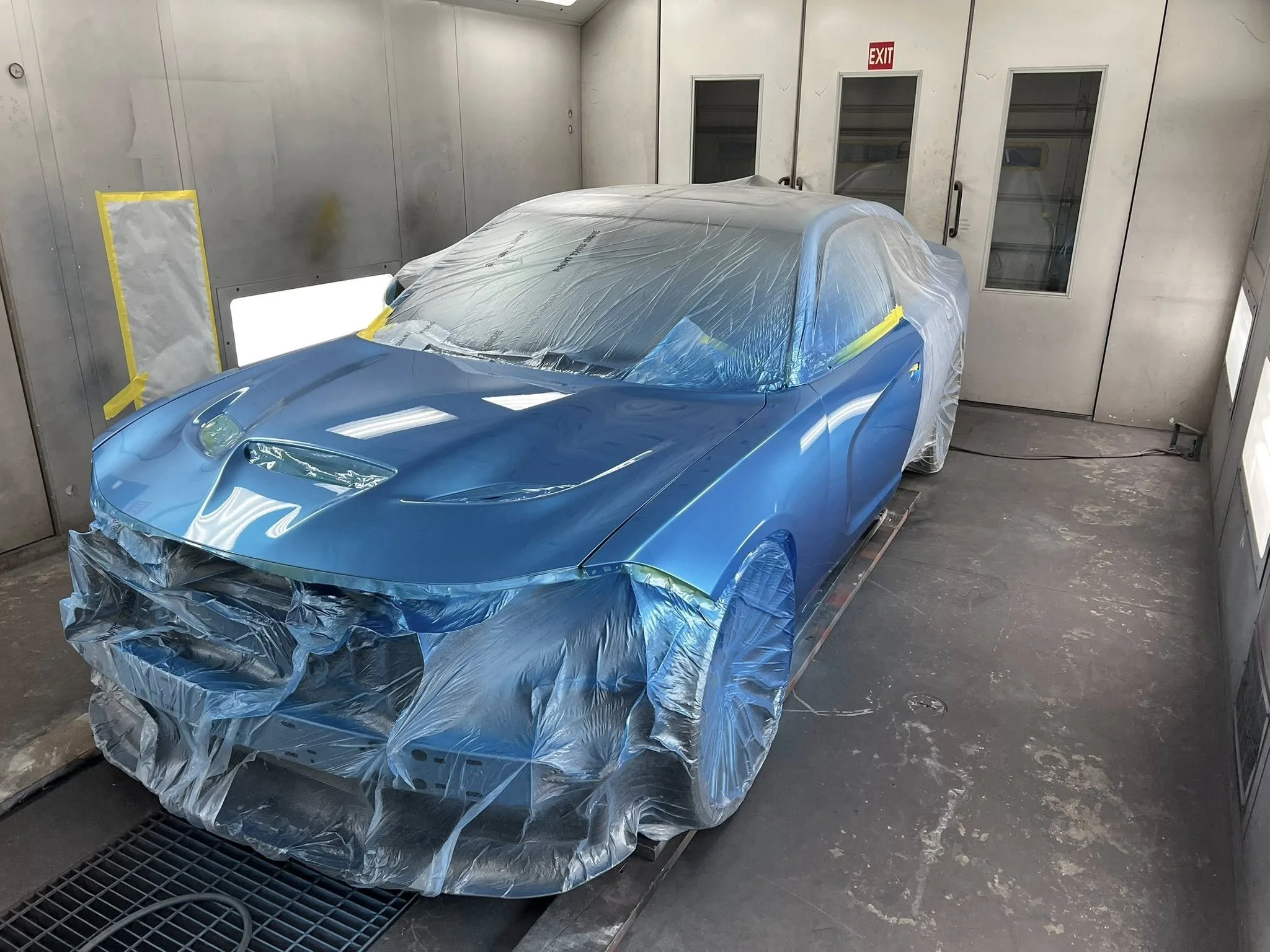 A blue sports car inside a paint booth, covered partially with plastic sheeting for a paint job.