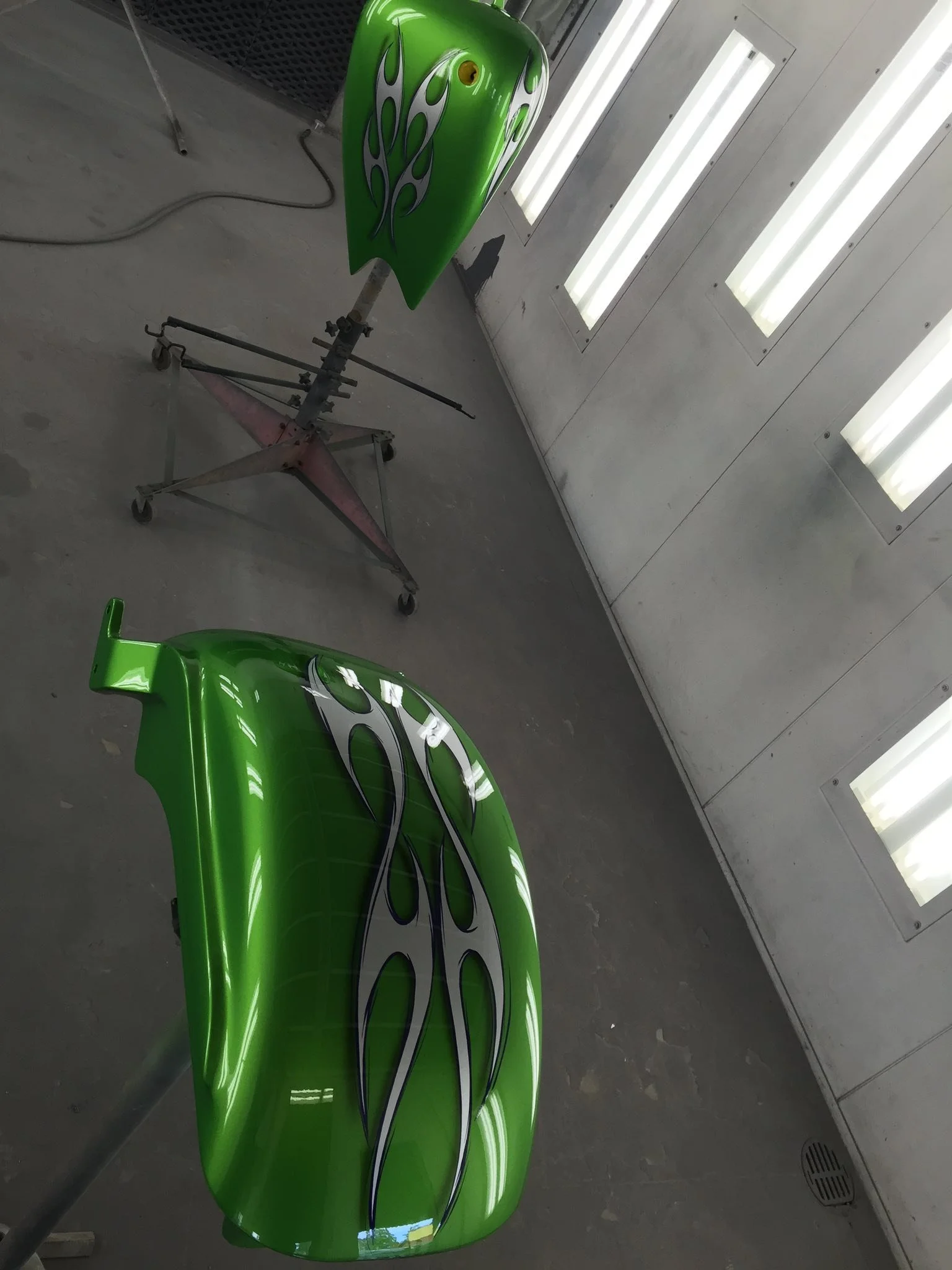 Green motorcycle fairings with black and white flame designs in a spray booth.