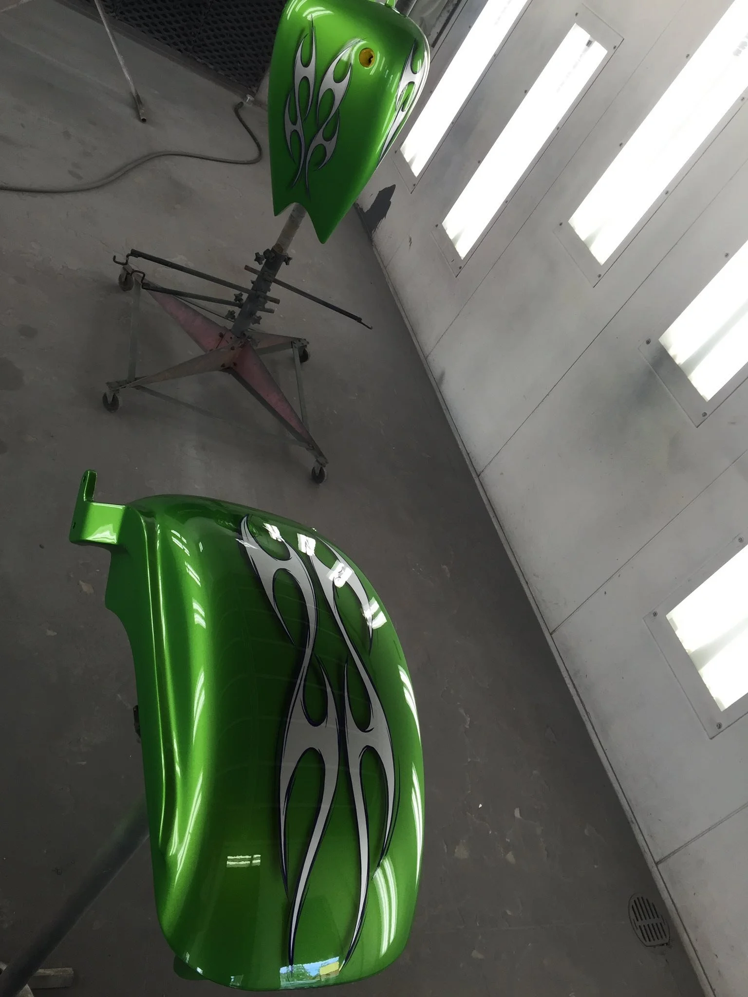Two flashing green car body parts with white and black flame decals, placed on stands in a workshop.
