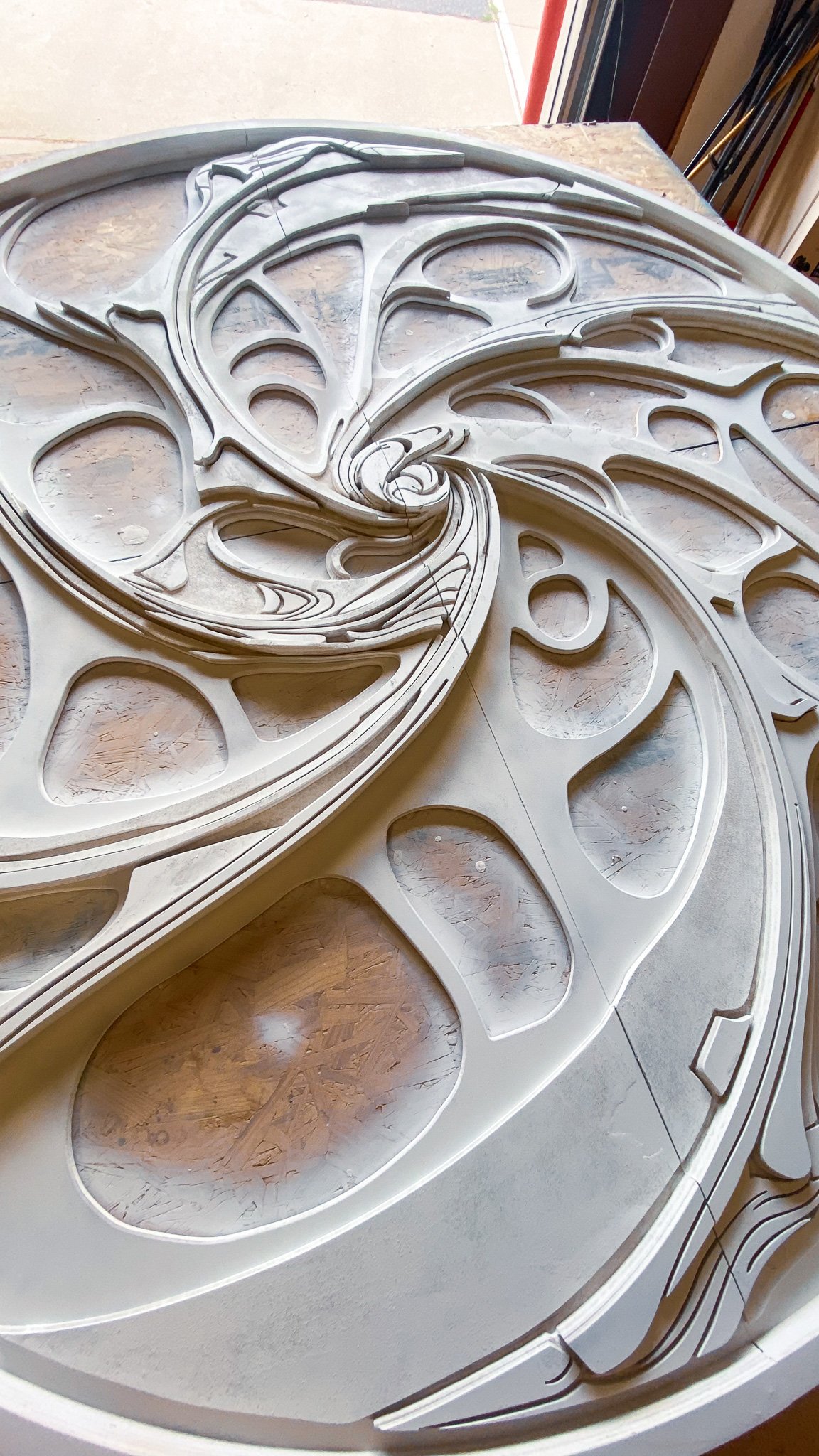 Wooden intricate decorative piece with swirling patterns and carved details, lying on a wooden surface.